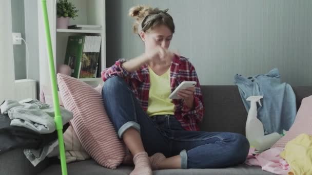 Beautiful young woman is resting on the sofa after cleaning and using the phone - Imágenes, Vídeo