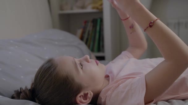 Little girl cute plays in smartphone lying on the bed - Video, Çekim