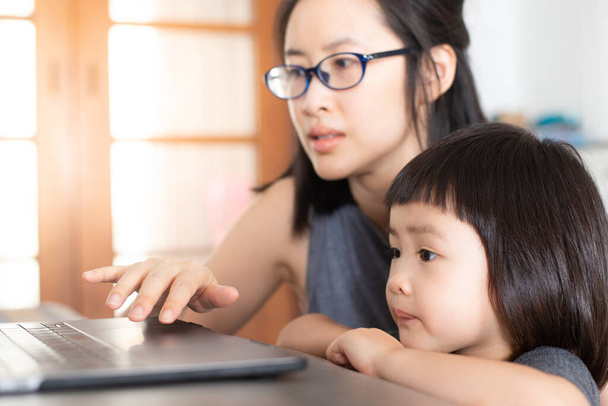An Asian girl is learning online lessons from a notebook computer with her mother, which may be new normal in the future. To prevent infection during the Covid-19 epidemic. - 写真・画像