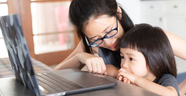 An Asian girl is learning online lessons from a notebook computer with her mother, which may be new normal in the future. To prevent infection during the Covid-19 epidemic. - Foto, Imagem