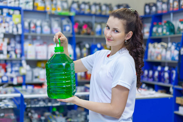 Jong meisje verkoopster biedt een fles van niet-vries reinigingsvloeistof voor het wassen van de voorruit van een auto in een auto-onderdelen winkel - Foto, afbeelding