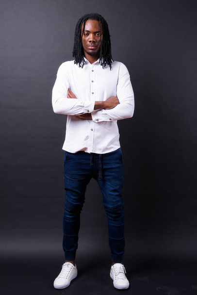 Studio shot of young handsome African businessman with dreadlocks against black background - Photo, image
