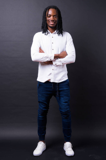 Στούντιο πλάνο του νεαρού όμορφου Αφρικανού επιχειρηματία με dreadlocks σε μαύρο φόντο - Φωτογραφία, εικόνα