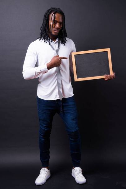 Studio shot of young handsome African businessman with dreadlocks against black background - Foto, immagini
