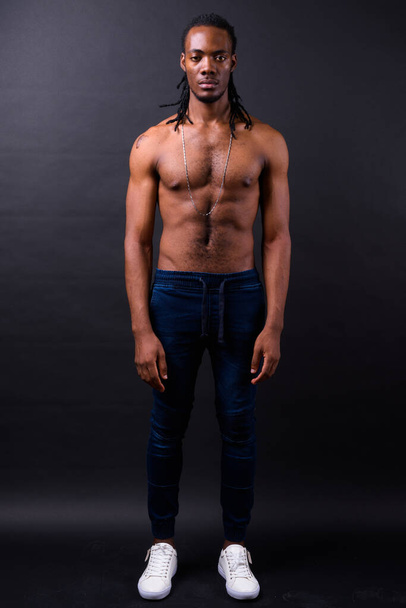 Студийный снимок молодого красивого африканца с дредами без рубашки на черном фоне - Фото, изображение