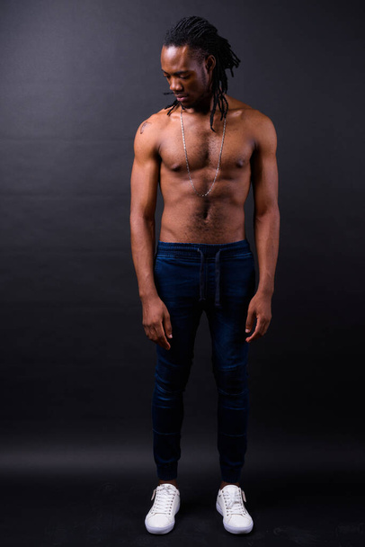 Studio shot of young handsome African man with dreadlocks shirtless against black background - Foto, afbeelding