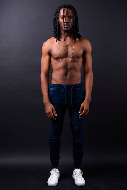 Studio shot of young handsome African man with dreadlocks shirtless against black background - Fotó, kép