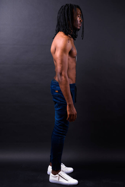 Studio shot of young handsome African man with dreadlocks shirtless against black background - 写真・画像