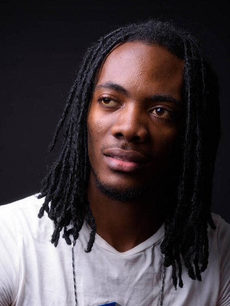 Studio shot of young handsome African man with dreadlocks against black background - Photo, image