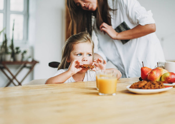 Jeune mère brosse les cheveux de sa petite fille pendant le petit déjeuner à table à la maison, routine du matin
 - Photo, image