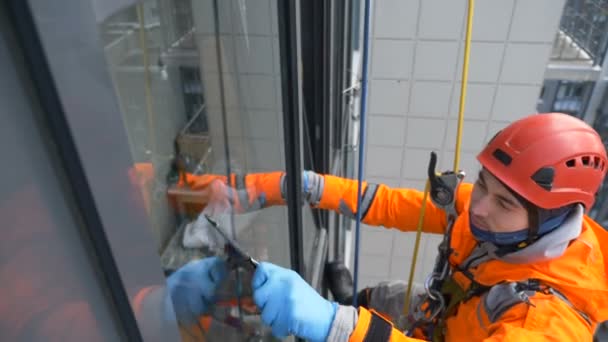 equipped window washer in helmet and overalls washes glass with screed at high altitude of building, slow motion - Footage, Video