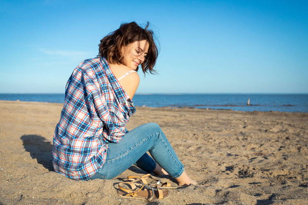 Atmospheric lifestyle photo of young beautiful woman  in shirt and jeans in on the beach.The concept of the unity of women and nature, peaceful mood, eco-friendly life - Photo, Image
