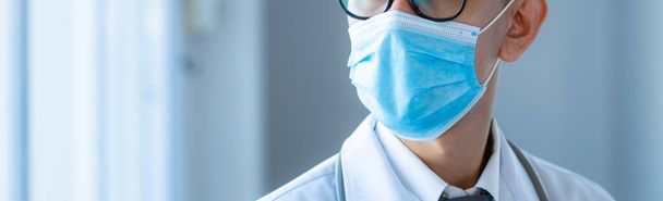 コロナウイルスに対する保護フェイスマスクを身に着けているクローズアップアジアの医師。医療スタッフ予防用具。新しい正常な背景の旗の医療 - 写真・画像