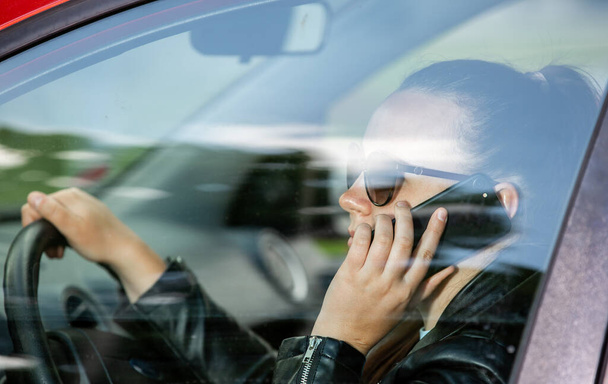 Pretty young woman using a smart phone, mobile while driving a car, transportation concept - Photo, Image
