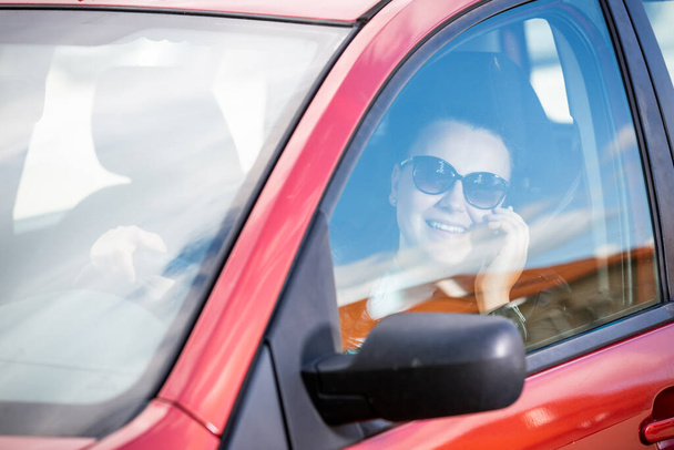 Pretty young woman using a smart phone, mobile while driving a car, transportation concept - Zdjęcie, obraz