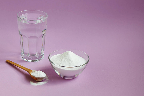 Collagen protein powder in spoon and jar, a glass of water on purple background. Natural beauty and health supplement for skin, bones, joints. - Foto, imagen