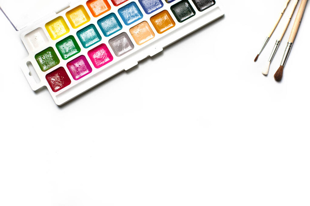 A palette of eighteen-color watercolors and paintbrushes on a white background with space for text. Children's creativity, creative classes with children at home and at school, art master class, the concept of creative development. - Photo, image