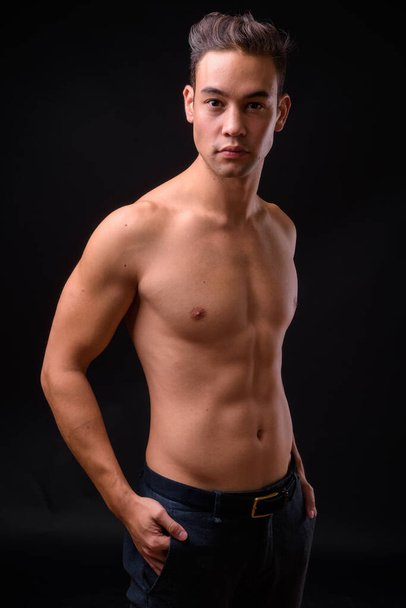 Studio shot of young handsome multi ethnic man shirtless against black background - Foto, Imagem