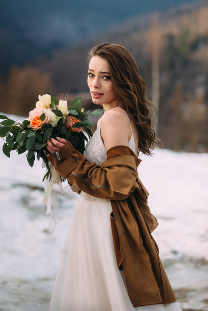 tender beautiful bride with a bouquet of flowers is standing in the forest. bride in a snowy forest. - Φωτογραφία, εικόνα