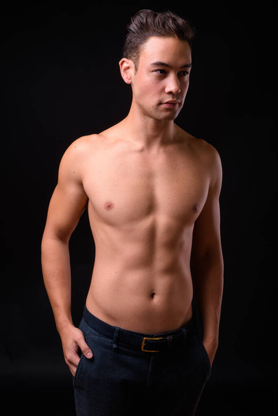 Studio shot of young handsome multi ethnic man shirtless against black background - Photo, image