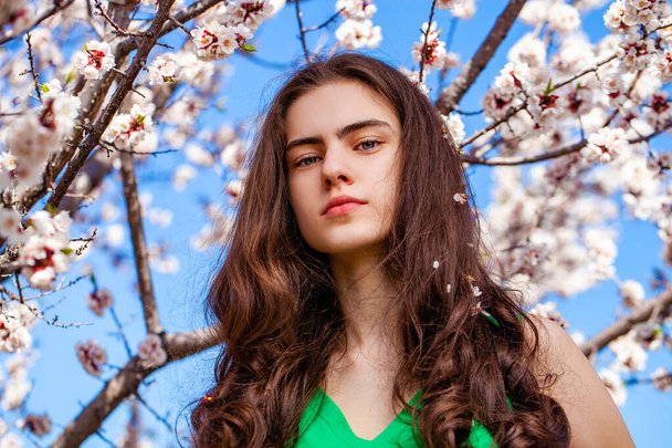Pretty teen girl are posing in garden near blossom cherry tree with white flowers. Spring time  - Valokuva, kuva