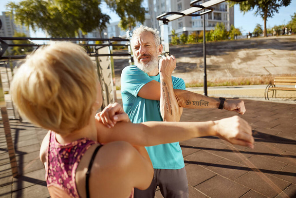 Physically active in any age. Athletic mature family couple in sportswear doing stretching exercises in the early morning outdoors, aged couple doing sport together - Photo, Image