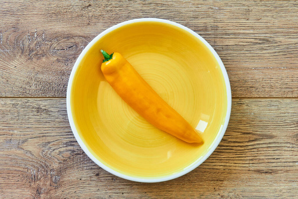color bodegón - vaina amarilla de pimiento dulce en un plato amarillo sobre una mesa de madera
 - Foto, imagen