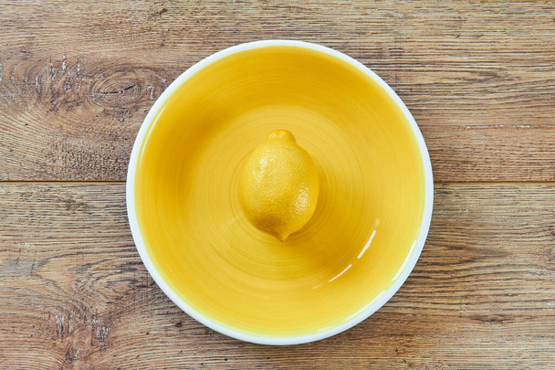 color still life - bright yellow lemon on a yellow plate on a wooden tabletop - Φωτογραφία, εικόνα