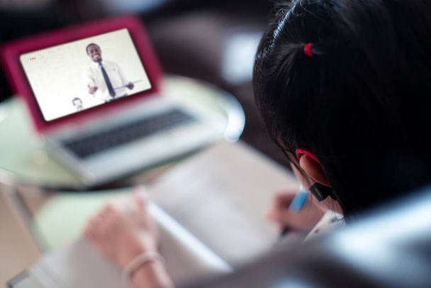 Κοριτσάκι που χρησιμοποιεί ακουστικά bluetooth για να μάθει στο laptop στο σπίτι, Κοινωνική απόσταση κατά τη διάρκεια της καραντίνας, Online εκπαιδευτική έννοια - Φωτογραφία, εικόνα