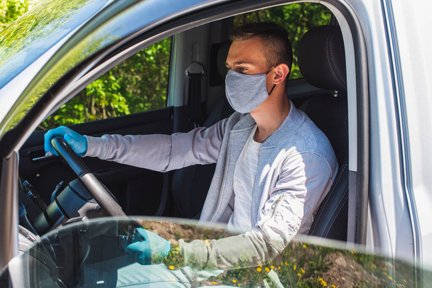 Quarantäne-Konzept. Pandemie. Ein junger Taxifahrer mit grauer Schutzmaske und grauer Jacke sitzt hinter dem Fahrersitz im Auto. Er schaut geradeaus. Virus. Coronavirus. Isolierung  - Foto, Bild