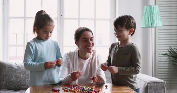 Young mixed race nanny teaching little kids creating handmade bracelets. - Materiał filmowy, wideo