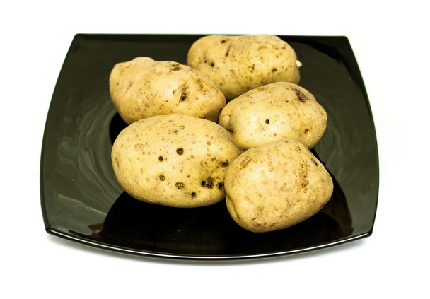 Raaka perunat mustalla lautasella
 - Valokuva, kuva