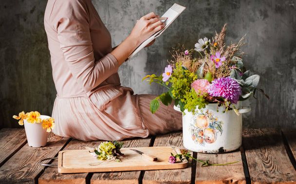 female artist draws a composition of wild flowers in a pot in a rustic style, a sketchbook on a table with pencils. Sketch art, artist inspiration, design, hobby, drawing school. hands close up - Photo, Image