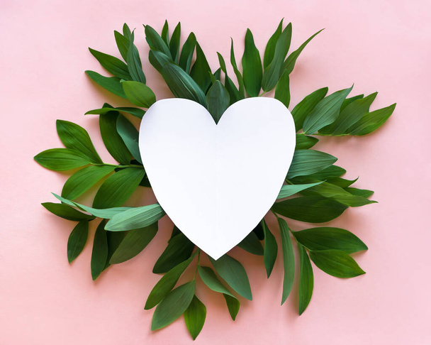 Creative layout of green leaves, wild plants on pink and white empty heart shape frame, copy space. Summer, spring or ecology design, love concept. - Photo, image