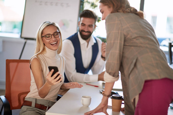 Young businesswoman showing her colleagues some images from her phone and smiling - Фото, изображение