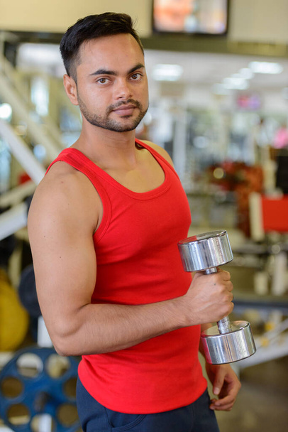 Portrait of young handsome bearded Indian man exercising at the gym - Zdjęcie, obraz