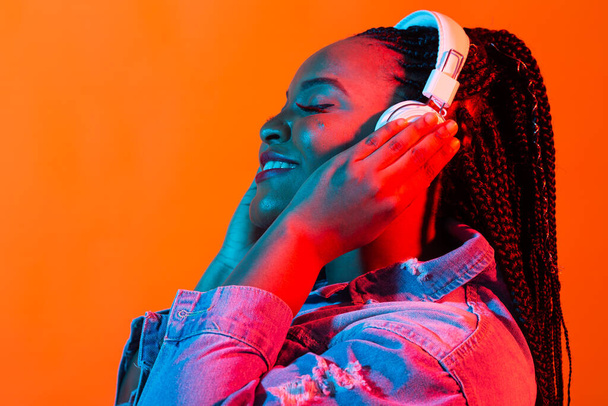 Neon portrait of young african woman listening music with earphones. - Photo, Image