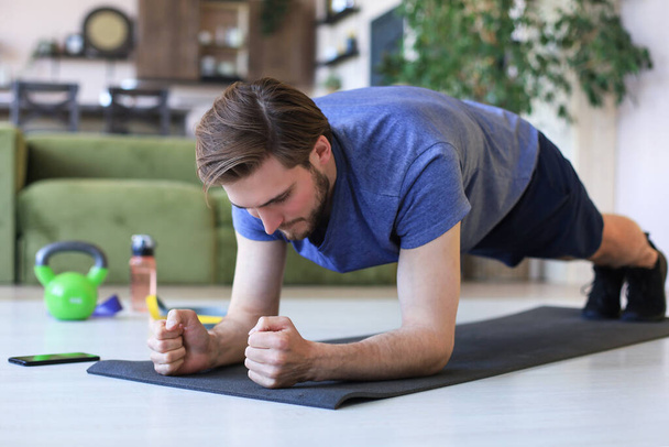 Attractive beared man doing plank exercise at home during quarantine. Fitness is the key to health - 写真・画像