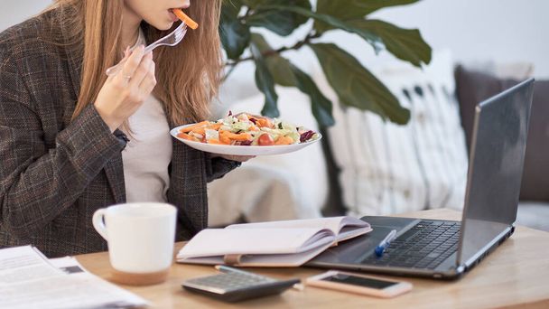 Onherkenbare jonge zakenvrouw met een lunchpauze aan het bureau, ze eet verse salade, persoon - Foto, afbeelding