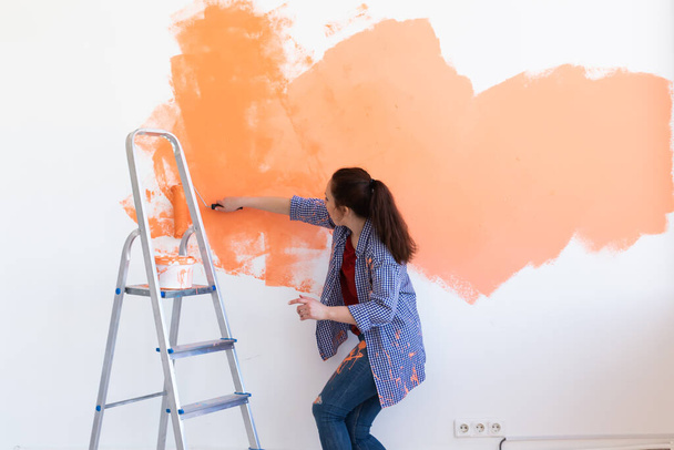 Dancing funny woman painting the walls of new home. Renovation, repair and redecoration concept. - Photo, Image