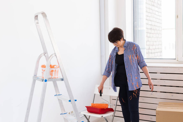 Ανακαίνιση, ανακαίνιση και επισκευή έννοια - μεσήλικες γυναίκα ζωγραφική τοίχο στο νέο σπίτι. - Φωτογραφία, εικόνα
