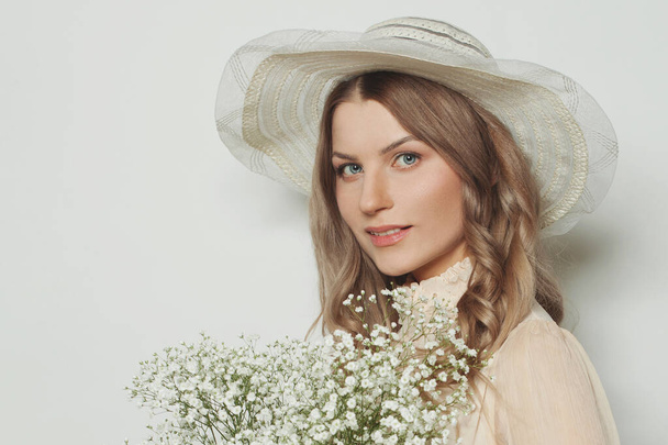 Femme blonde joyeuse en chapeau tenant des fleurs, portrait rapproché
 - Photo, image
