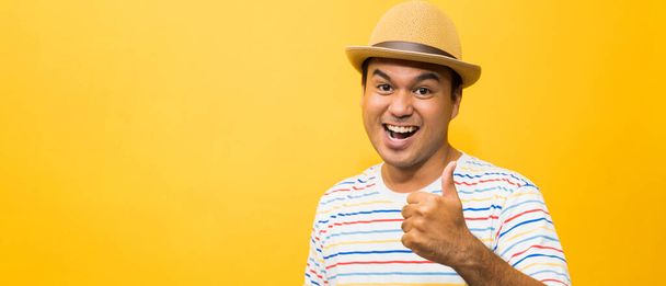 Young Asian man with hat feels happy  and surprise and showing thumb up on yellow background. - Photo, Image