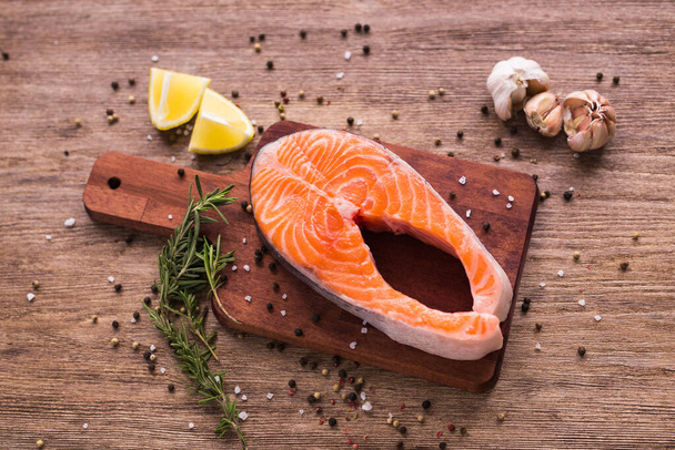 Raw salmon steak on wooden board top view. Healthy food, diet and mediterranean cuisine concept - Photo, Image