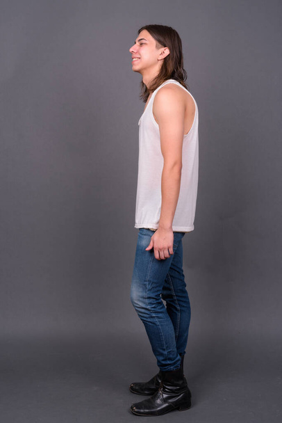 Студійний знімок молодого красивого андрогінного чоловіка з довгим волоссям на сірому фоні
 - Фото, зображення