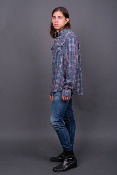 Студийный снимок молодого красивого андрогинного хипстера с длинными волосами на сером фоне - Фото, изображение