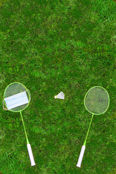 Coronavirus protection sing. Badminton rackets and shuttlecock on green grass. Medical mask on one racket. view from above - Fotoğraf, Görsel