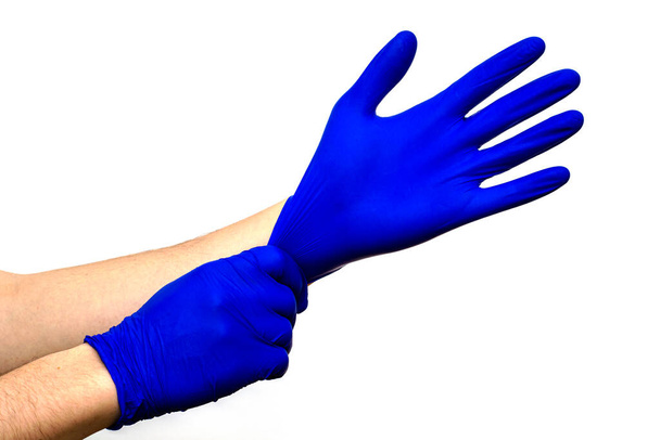homem coloca em suas mãos luvas de proteção de borracha cirúrgica azul em um fundo branco
 - Foto, Imagem
