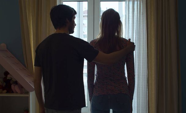 Σιλουέτα ζευγαριών κοντά στο παράθυρο. Ο σύζυγος βάζει το χέρι του στον ώμο της συζύγου σε αναζήτηση της συμφιλίωσης. - Φωτογραφία, εικόνα
