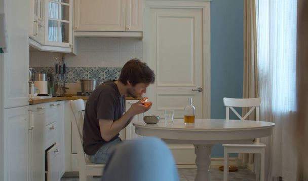 A drunk man lights a cigarette. Man drinking alcohol at home in the kitchen - Photo, Image